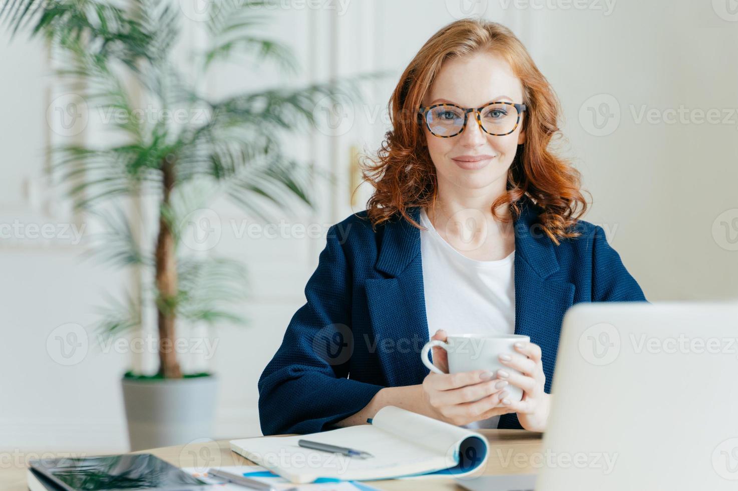 mujer independiente elegante de aspecto agradable libros artículos en la tienda web, lee noticias en Internet, escribe notas en el bloc de notas, trabaja en una computadora portátil, vestida con un traje elegante. concepto de negocio y trabajo foto