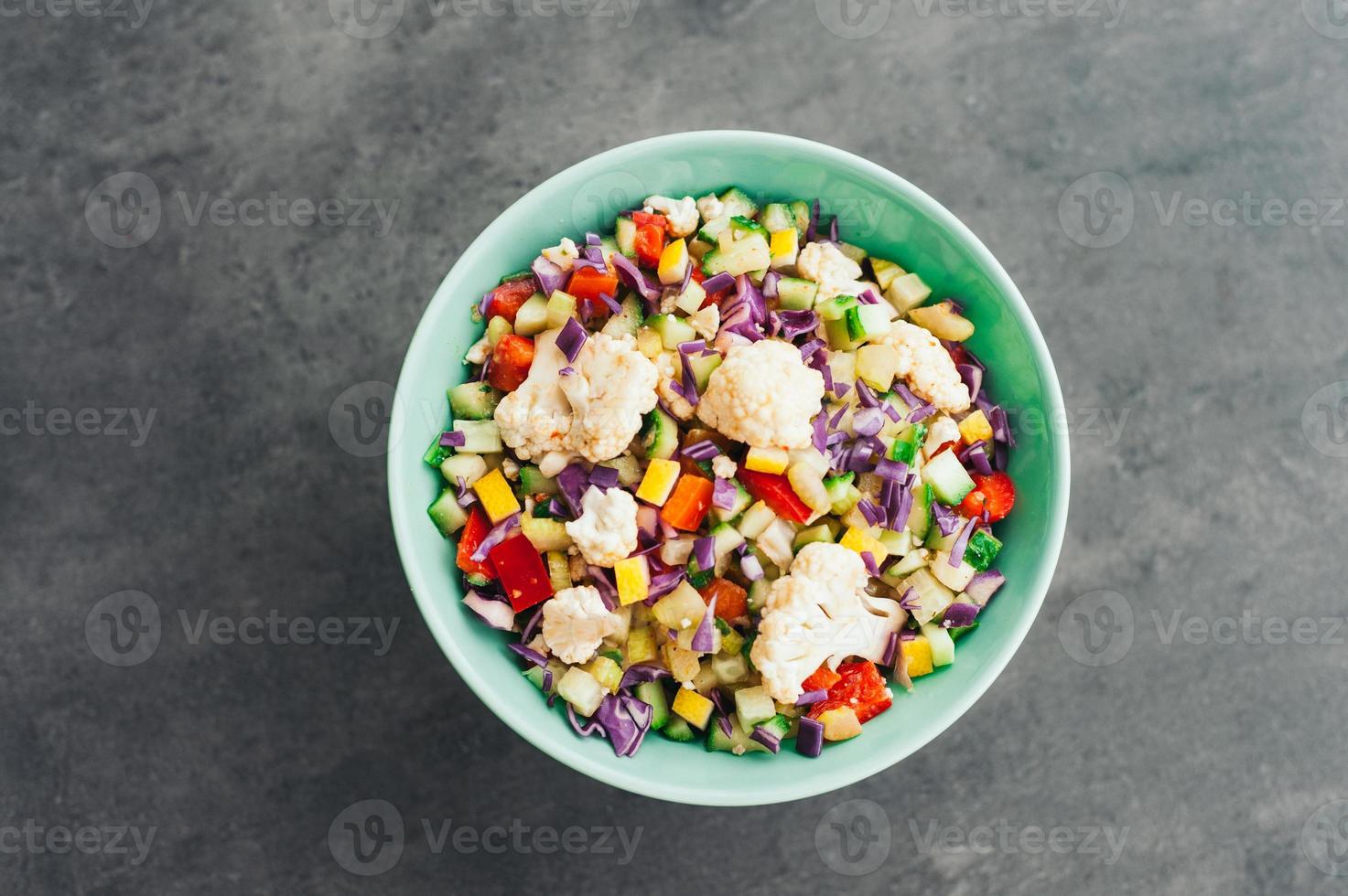 vista superior de ensalada de verduras frescas con coliflor, col morada, pimiento rojo picado y pepino. deliciosa comida en un tazón. concepto de alimentación y nutrición foto