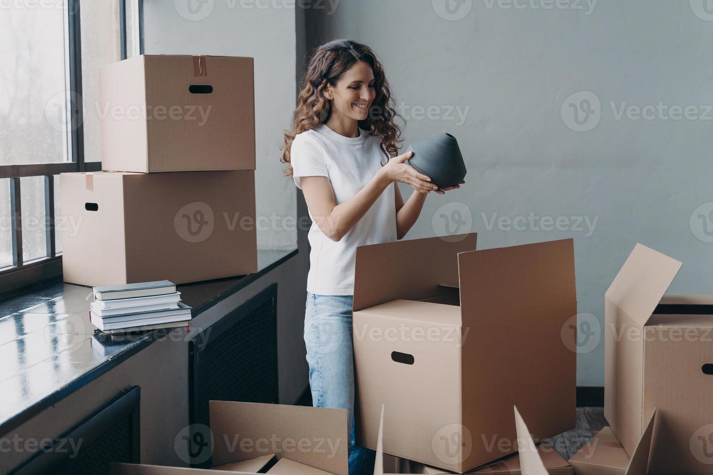 niña feliz desempacando cajas de cartón y tomando el jarrón. mujer europea empacando cajas para mudarse. foto