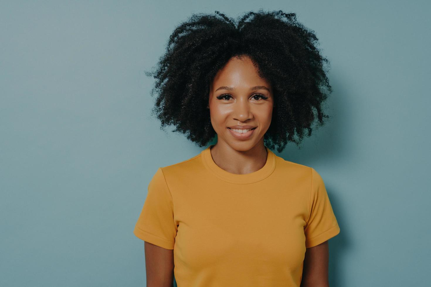 Waist up portrait of cheerful mixed race woman with curly hair posing in studio with happy smile photo