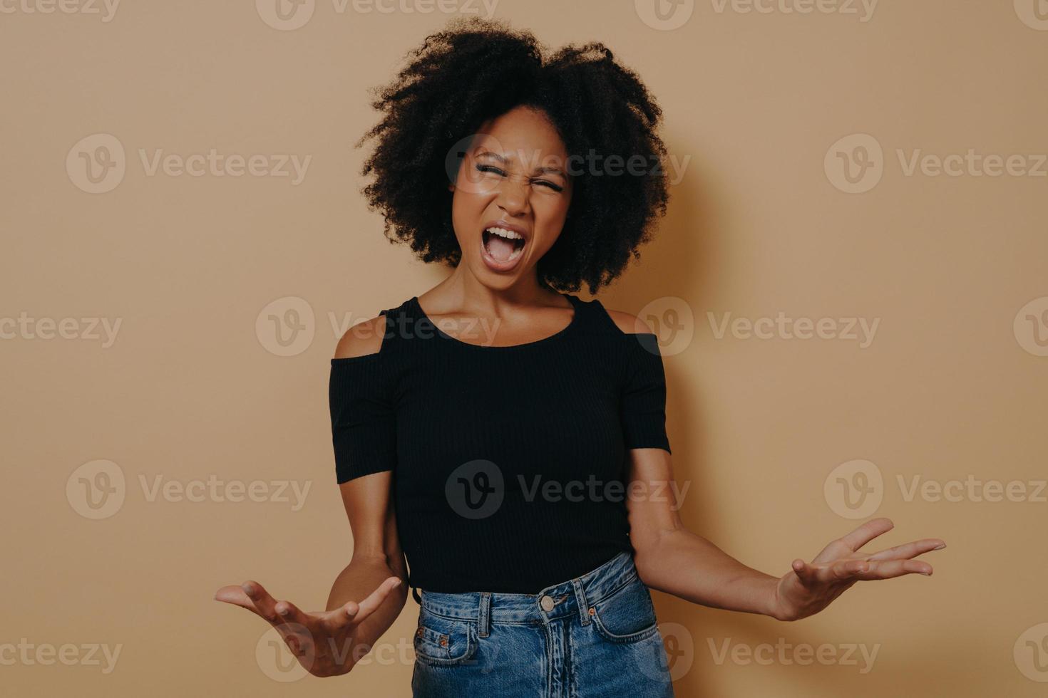 mujer africana con camiseta negra posando gritando, abriendo las palmas, sintiéndose enojada foto