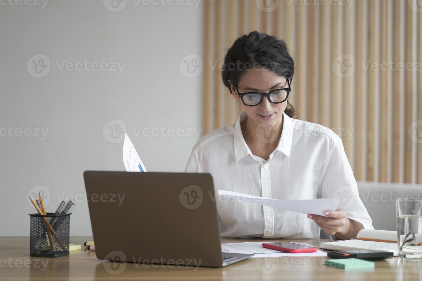 Young focused Italian businesswoman in formal wear analyzing documents, reading project statistics photo