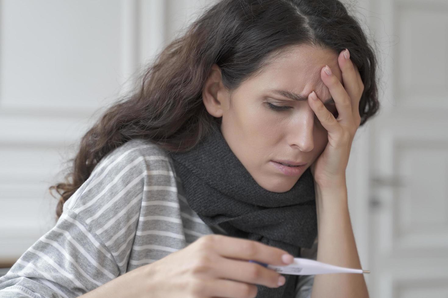 Sick diseased hispanic woman with headache measuring checking temperature at home photo