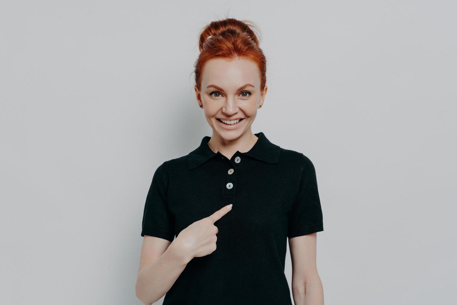 Young cheerful caucasian red haired woman pointing at herself while standing isolated over grey wall photo