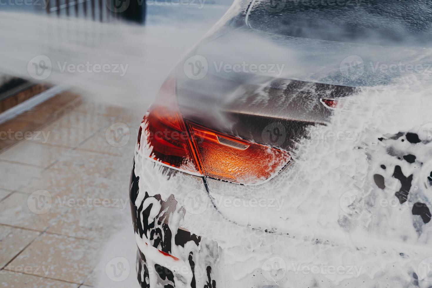 Washing car exterior surface with high pressure washer at self-serve cleaning station outdoors photo