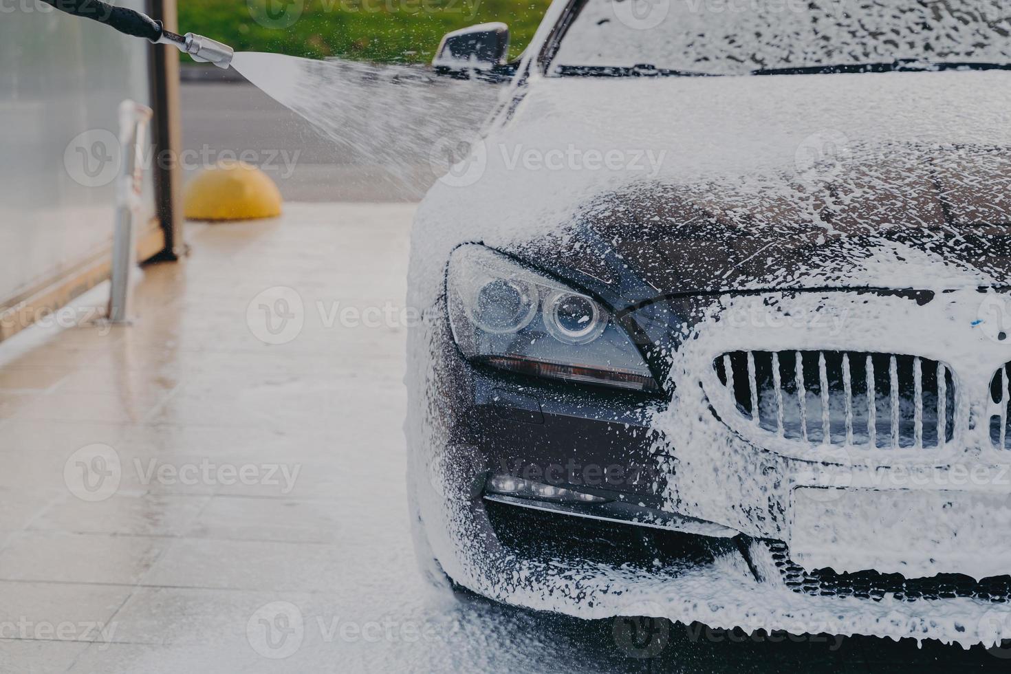 Car in white soap snow foam at carwashing center outdoors photo