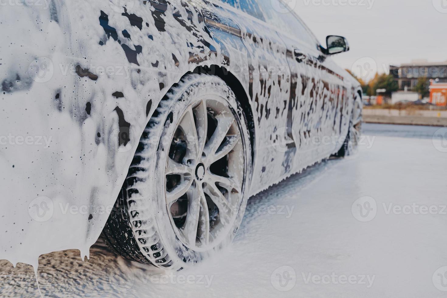 Vehicle in white soapy foam during regular car wash outdoors, auto getting wash with soap photo