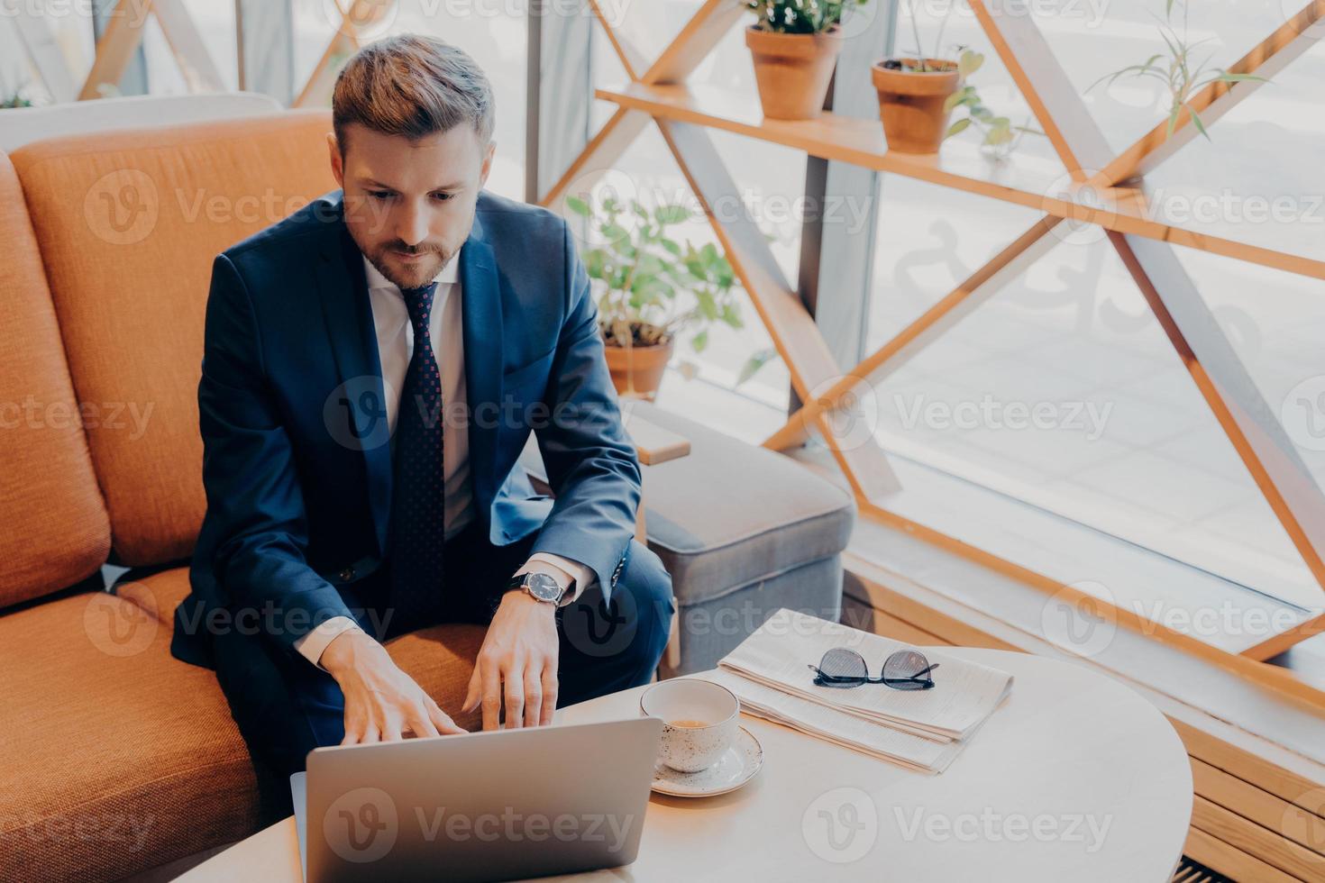 Successful well-groomed financier in stylish suit with trimmed beard sits in lobby photo