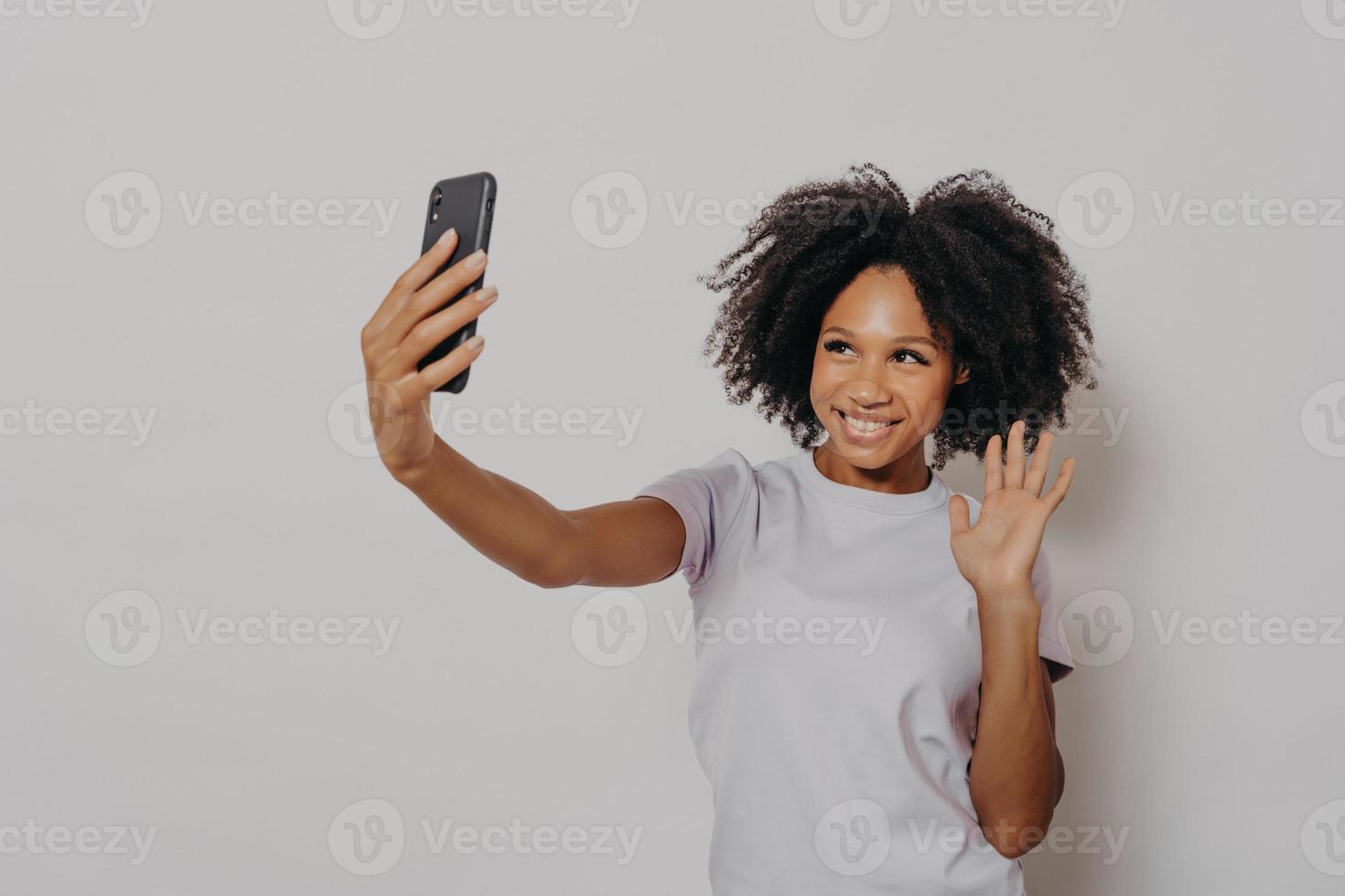 mujer joven feliz saludando a la cámara mientras hace una videollamada con su mejor amiga en un smartphone moderno foto