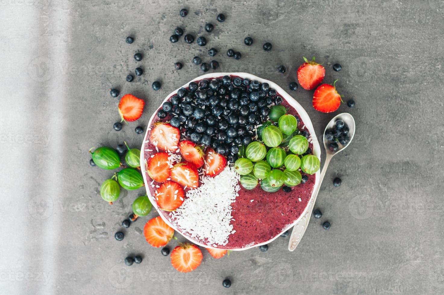 Ripe fruit on bowl. Strawberry, gooseberry and blueberry decorated with coconut flakes. High resolution product. Spoon with berries photo