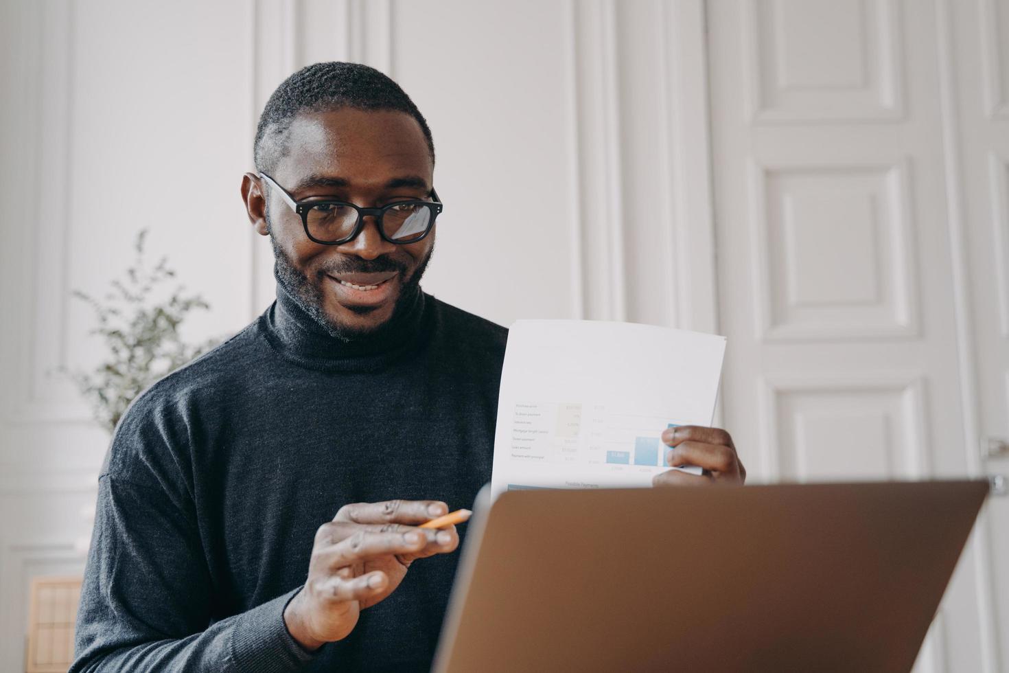 Positive young african american man freelancer having video conference with partner on laptop photo