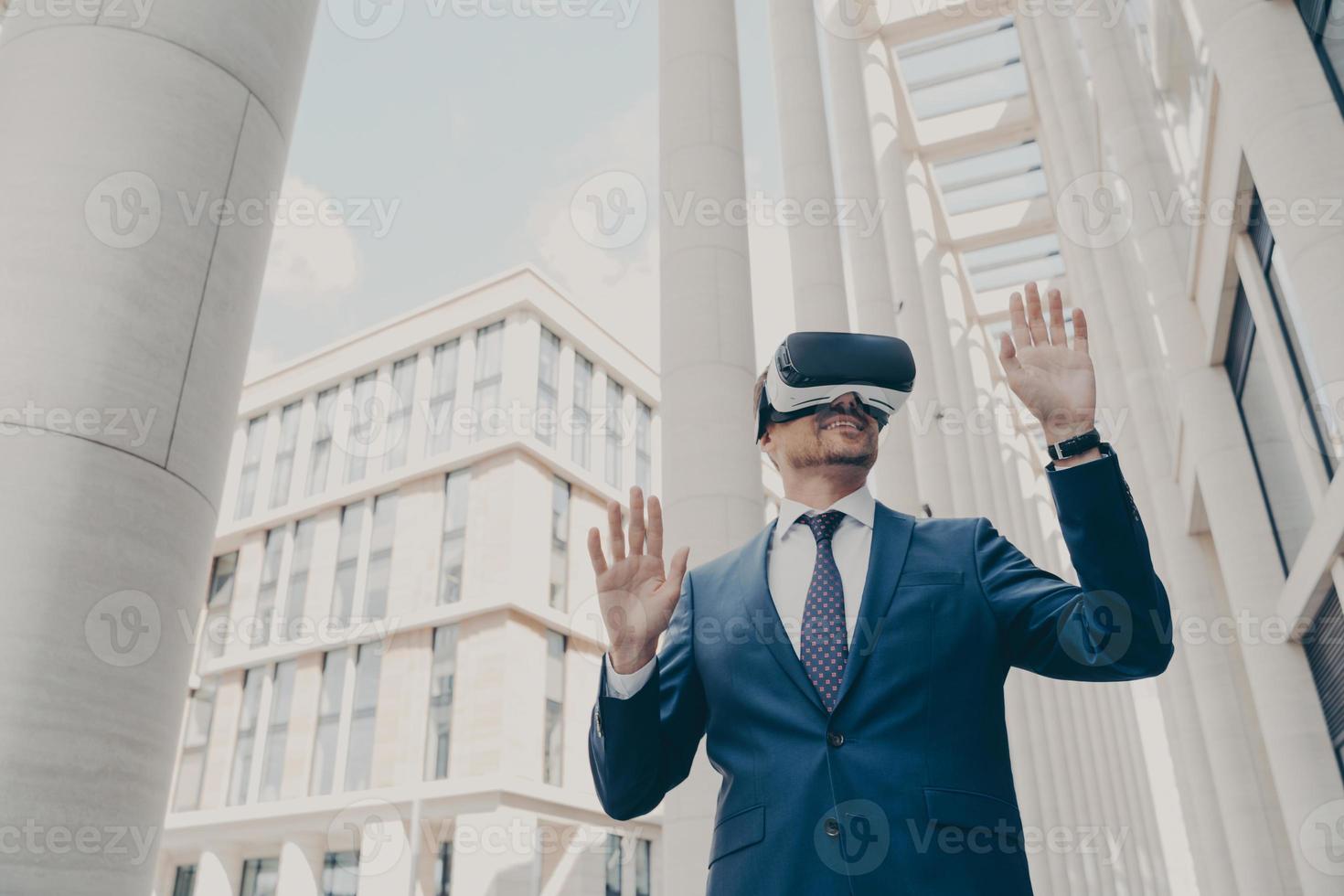 Futuristic image of happy businessman using virtual reality 3d goggles while standing outdoors photo