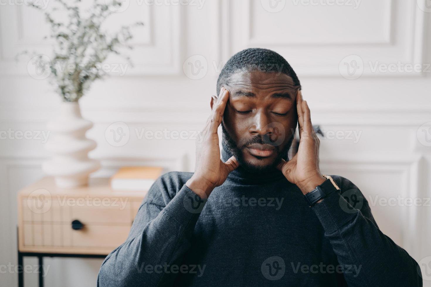 Stressed young african man employee with frustrated face expression suffering from headache photo