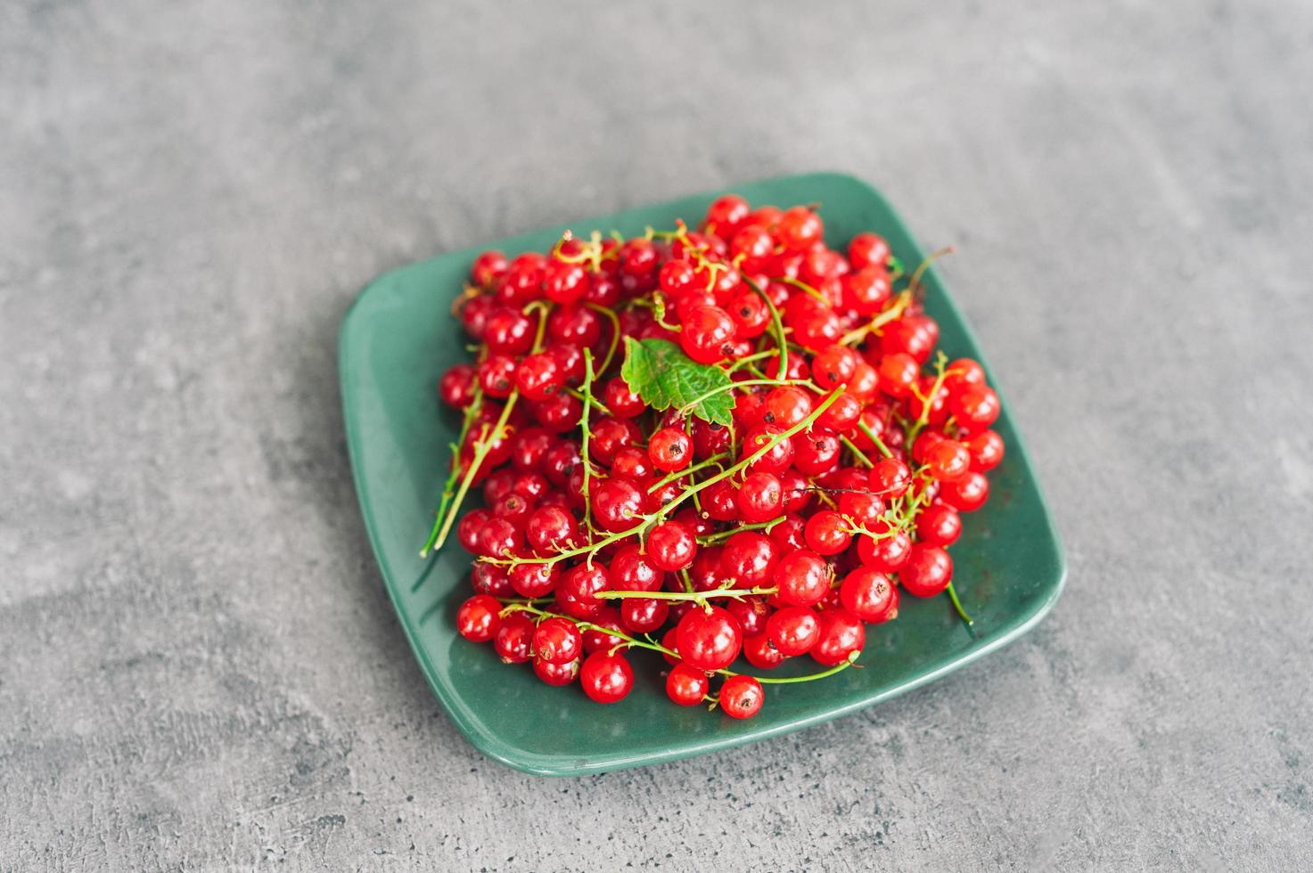 Tasty ripe red currant on plate at dark rustic table. Fresh summer berries. Fruit and vitamins. Healthy eating concept. Seasonal berries photo