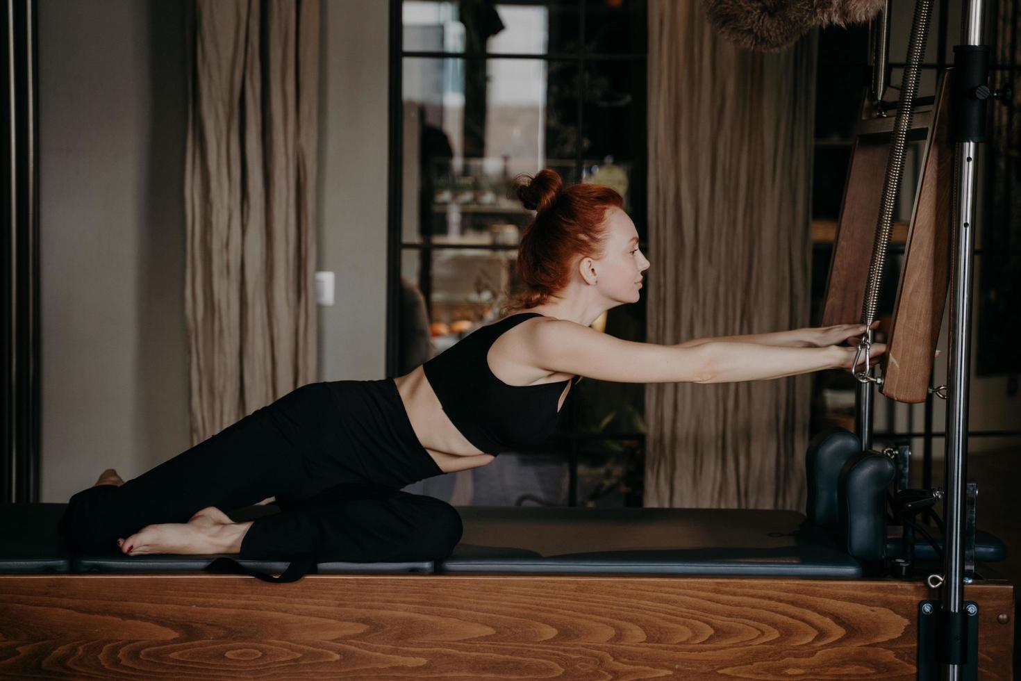 Red haired woman doing stretching routine on cadillac machine or trapeze table photo