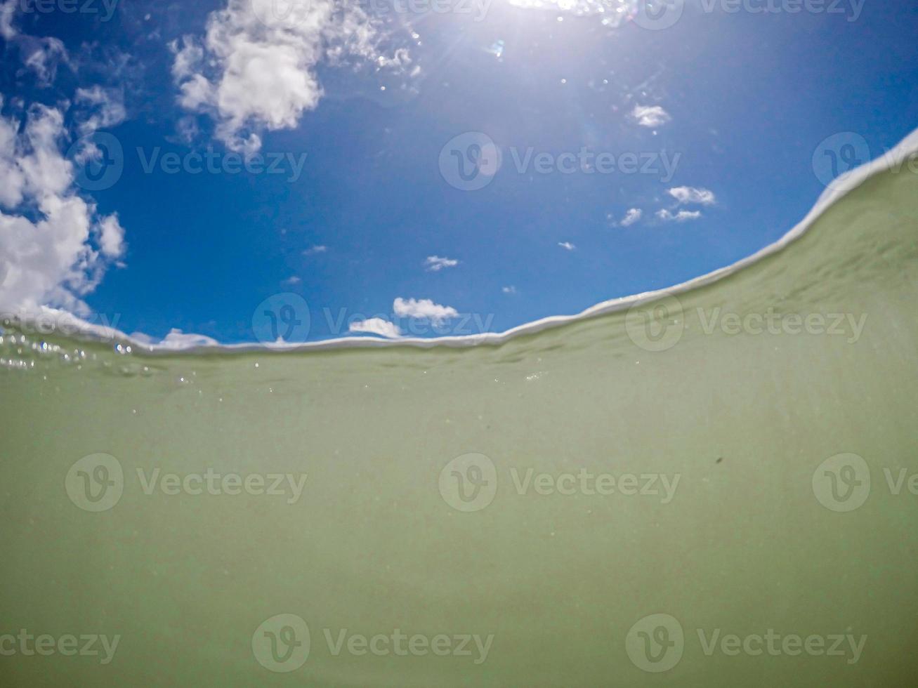 Underwater sea level photo of tropical exotic paradise bay with beautiful blue sky and clouds.