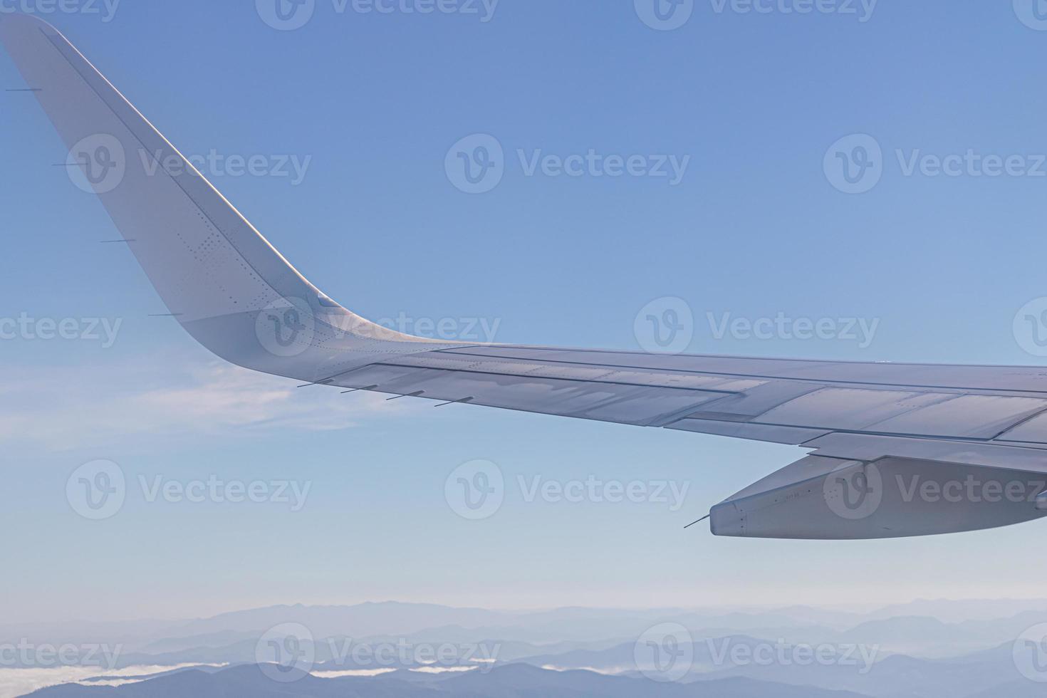 Wing of plane with beautiful sunrise skyline. Airplane flying on blue sky. View from airplane window. Commercial airline flight in the morning with sunlight. Plane wing above clouds. photo