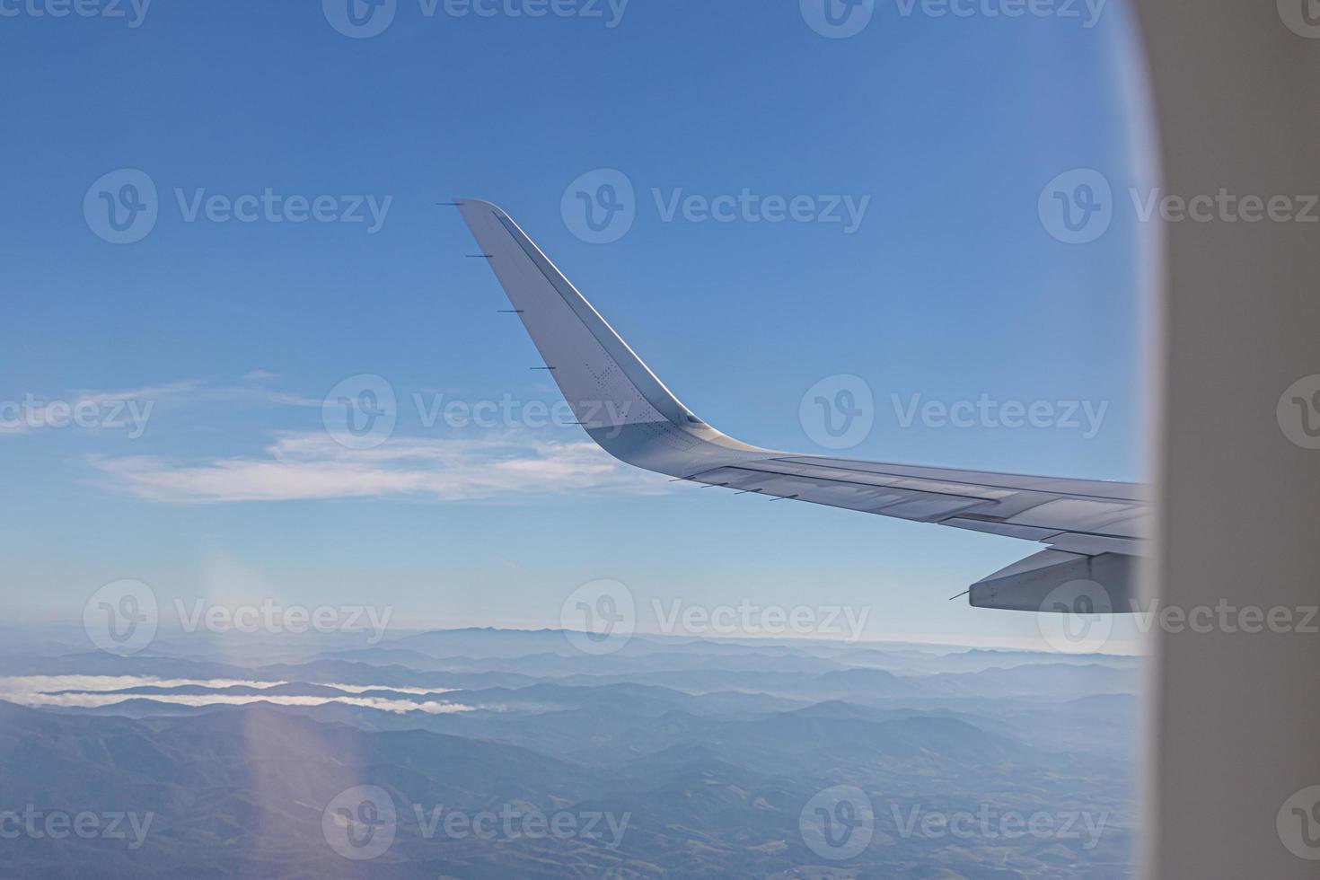 Wing of plane with beautiful sunrise skyline. Airplane flying on blue sky. View from airplane window. Commercial airline flight in the morning with sunlight. Plane wing above clouds. photo