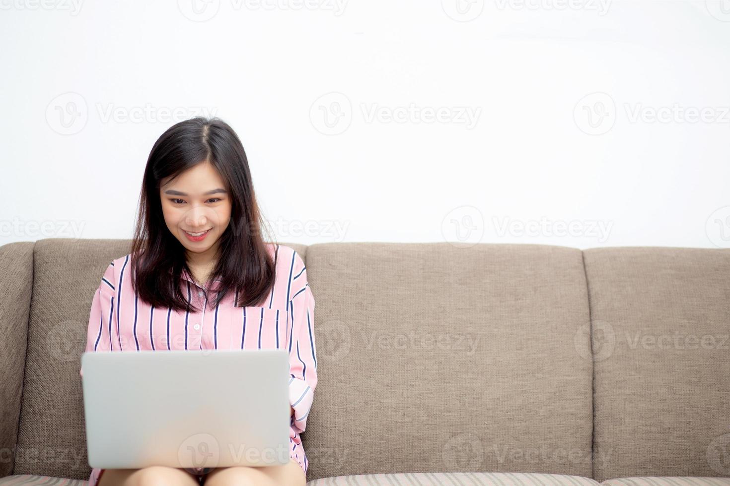 Beautiful of portrait asian young woman working online laptop sitting on sofa at living room, girl using notebook computer with connect to internet for distance job, business and success concept. photo