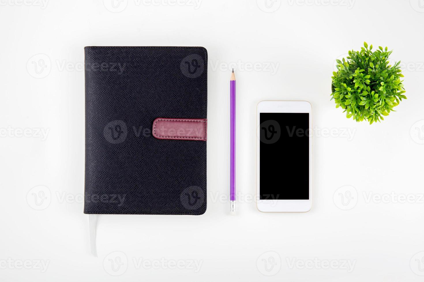 Black cover leather notebook or diary for reminder and memo isolated on white background, book mockup pencil tree and smart phone on desk office, education and supplies concept, top view. photo