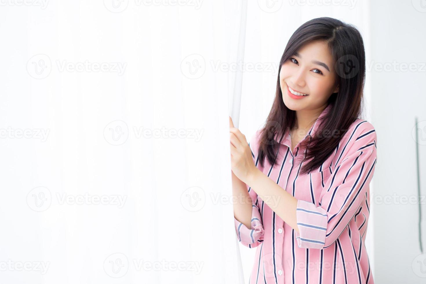 Portrait of beautiful young asian woman standing the window and smile while wake up with sunrise at morning, lifestyle and relax concept. photo