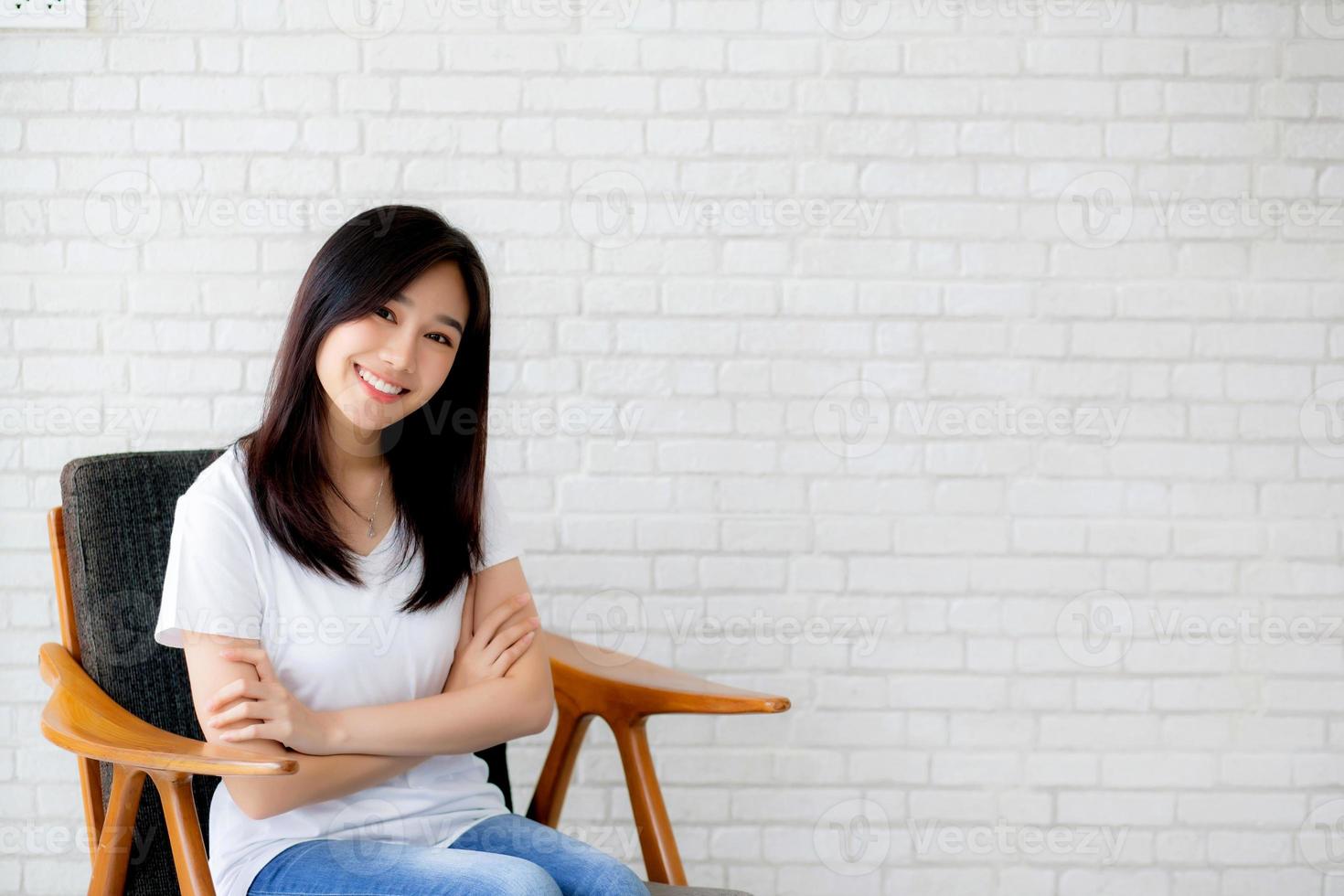 retrato de la felicidad de una hermosa joven asiática sentada en una silla sobre fondo de ladrillo de pared gris de textura de cemento, la mujer de negocios es una sonrisa en el concepto de personas de negocios concretas. foto