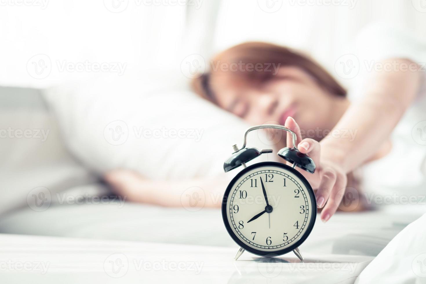 Beautiful asian young woman turn off alarm clock in morning, wake up for sleep with alarm clock, relax and lifestyle concept. photo