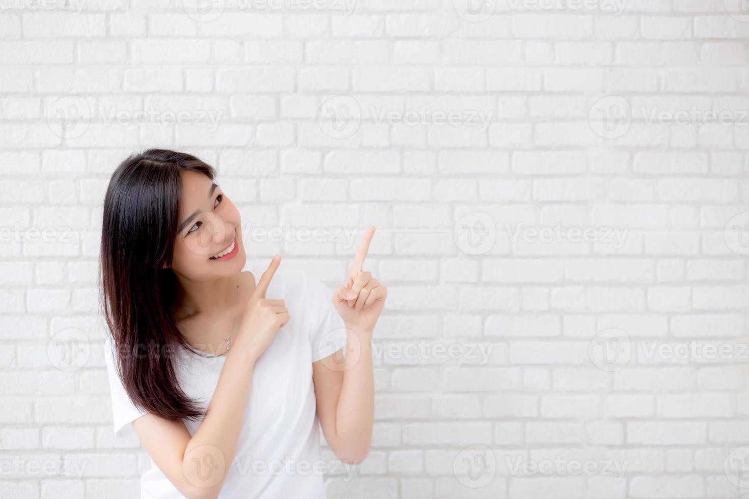 Portrait beautiful young asian woman happiness standing finger pointing something on gray cement texture grunge wall brick background, businesswoman is a smiling on concrete, business people concept. photo
