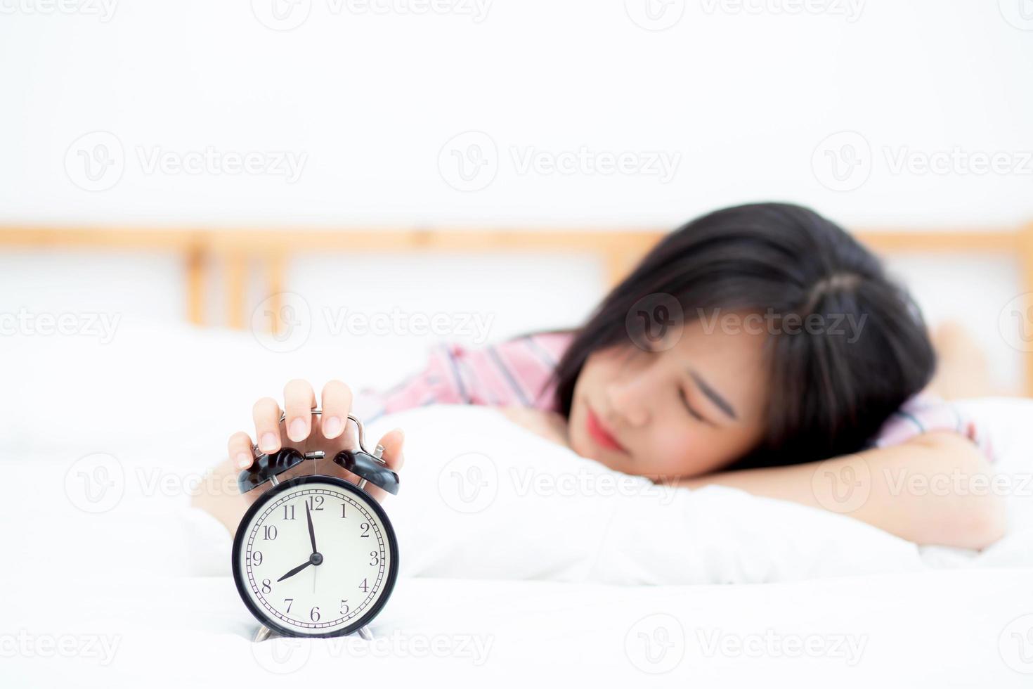 Beautiful asian young woman turn off alarm clock in morning, wake up for sleep with alarm clock, relax and lifestyle concept. photo