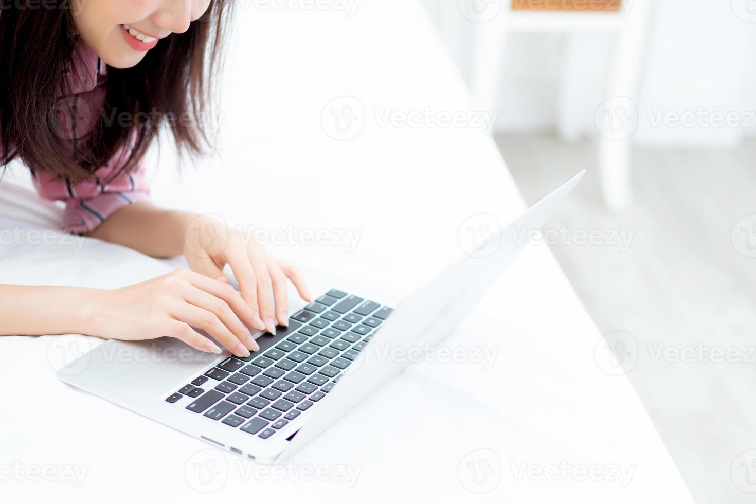 Beautiful asian young woman lying on bed using laptop at bedroom for leisure and relax, freelance with girl working notebook, communication concept. photo