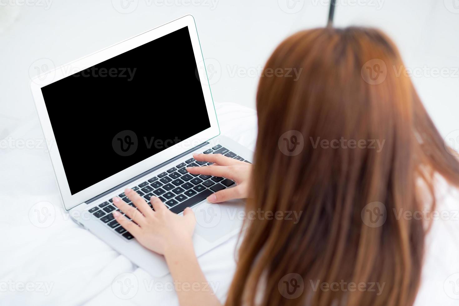 mujer asiática joven de primer plano que usa una computadora portátil para el ocio en el dormitorio, una chica que trabaja en línea con un portátil independiente, concepto de negocio, vista superior. foto