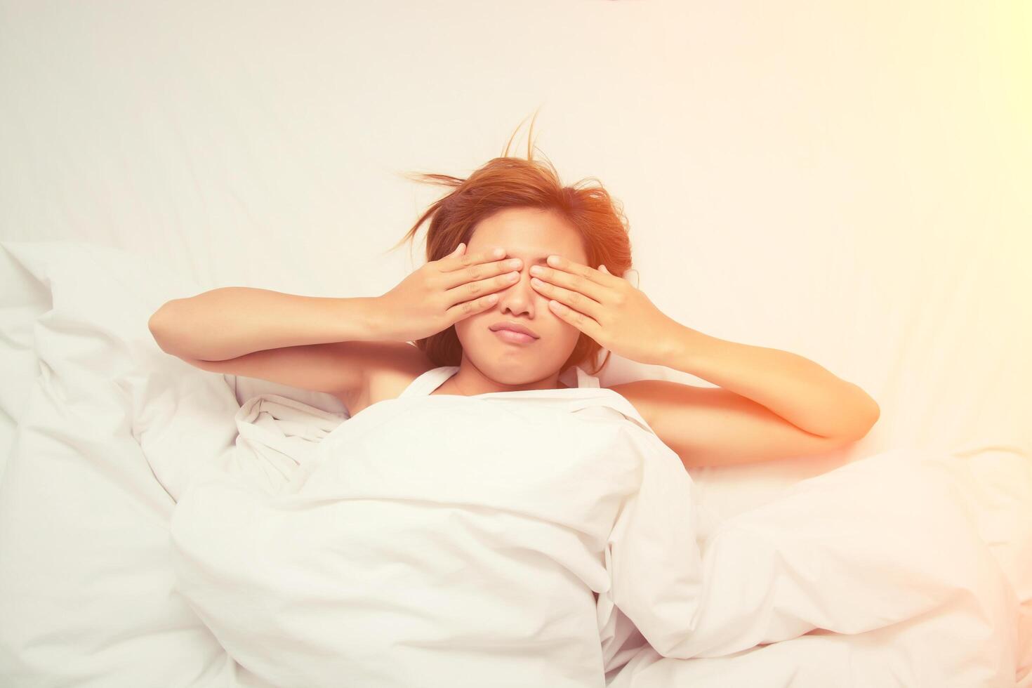 hermosa joven se quita las manos de la cara y frunce el ceño en la cama no quiere despertarse por la mañana foto