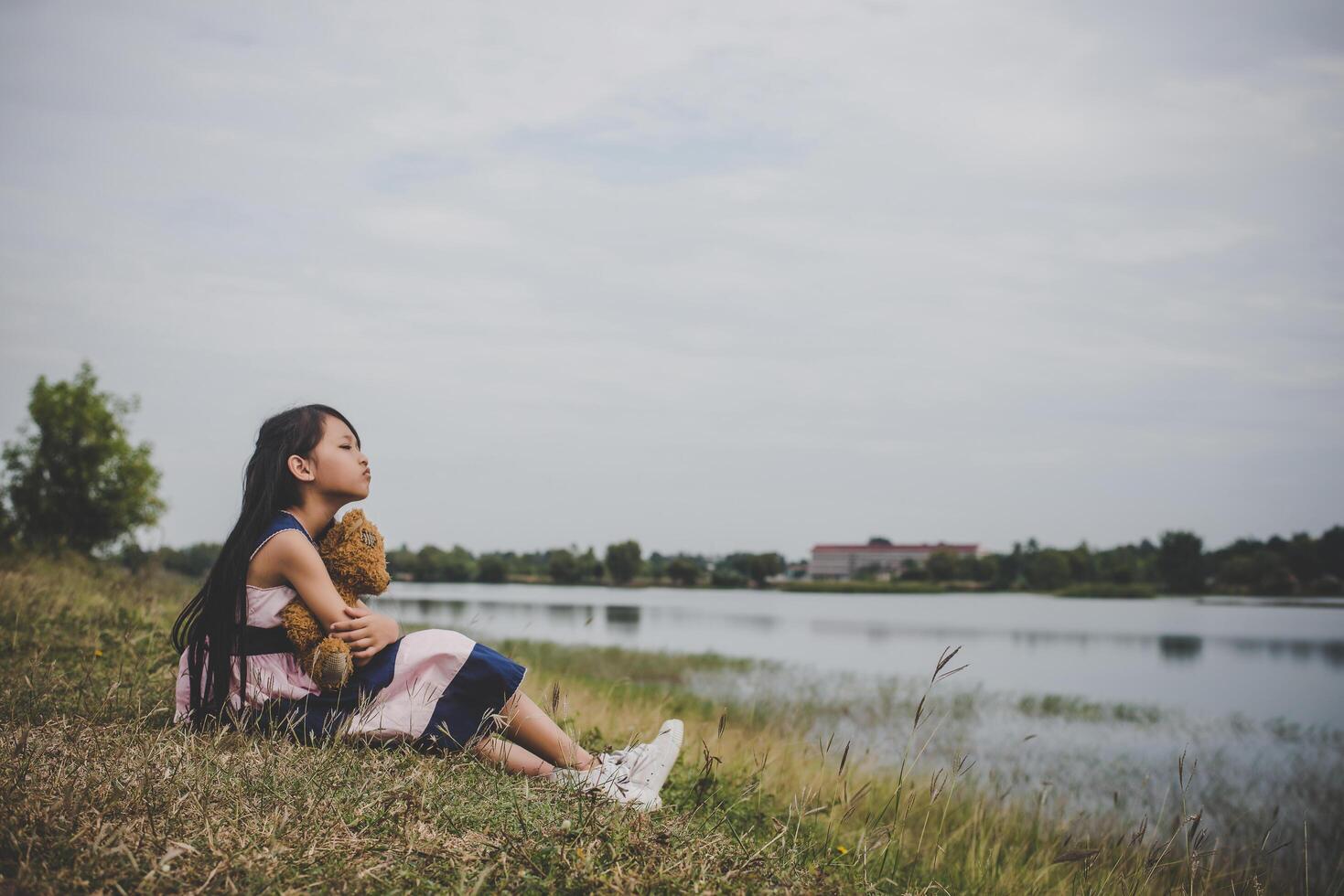 Little girl sitting with her bear upset at meadows field. photo