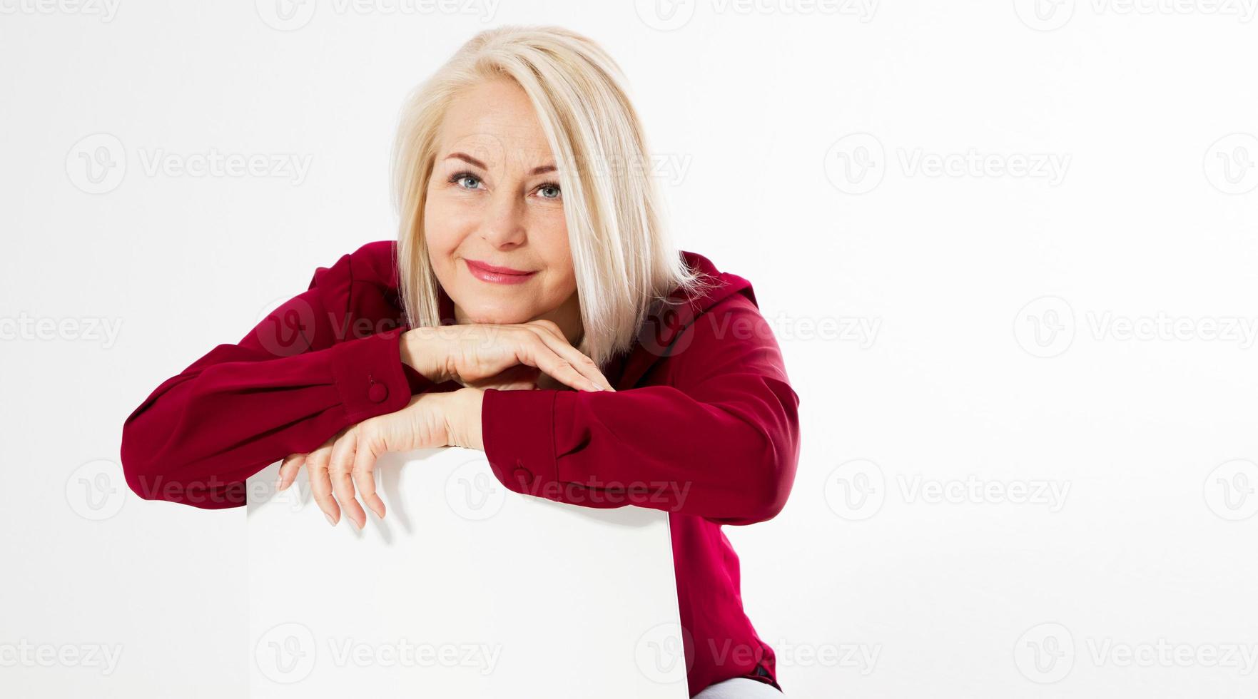 Portrait of smiling cheerful happy middle-aged blonde woman sitting on chair isolated on white photo