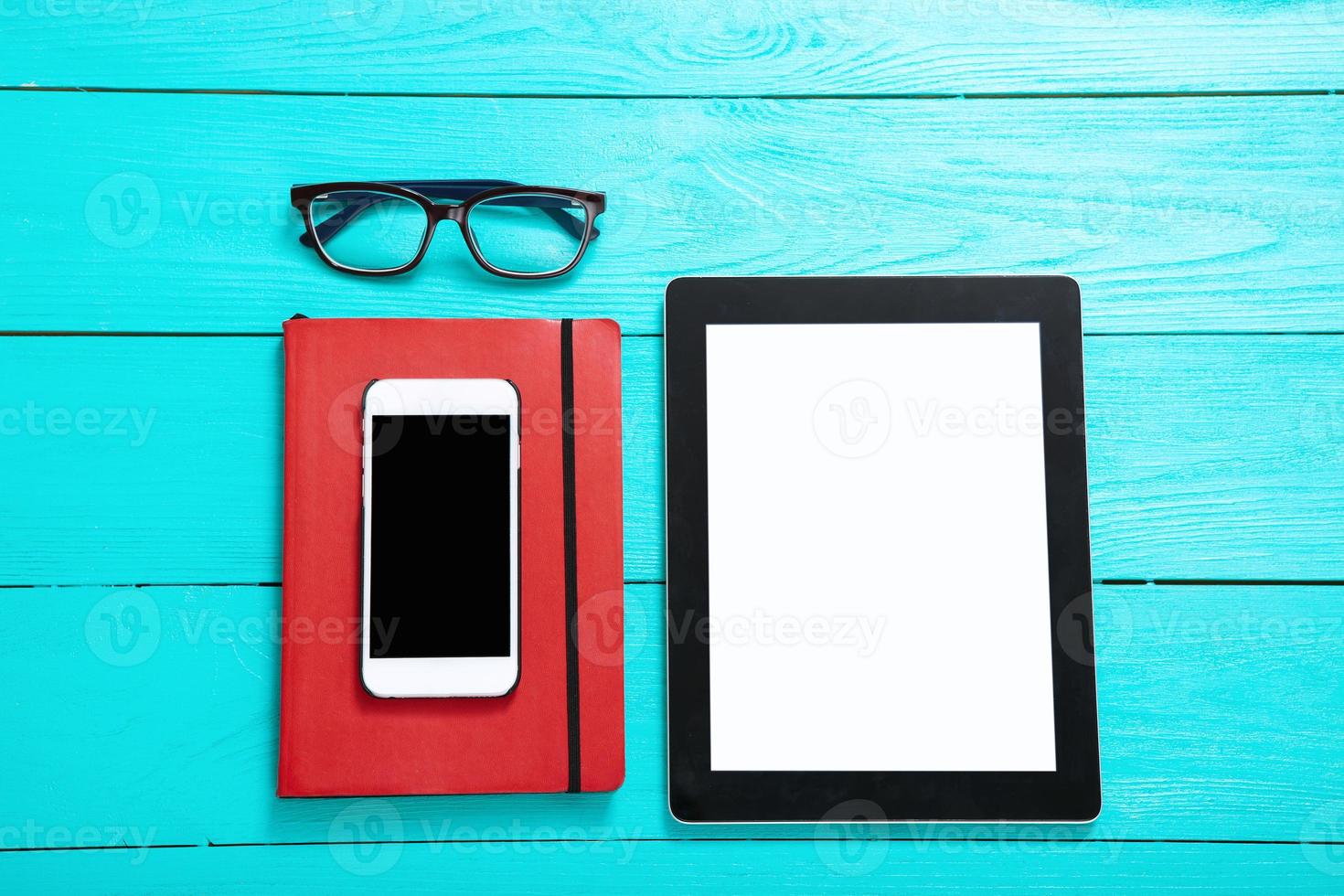 Electronic devices with places for text. Notebook and glasses. Blue wooden background and top view photo