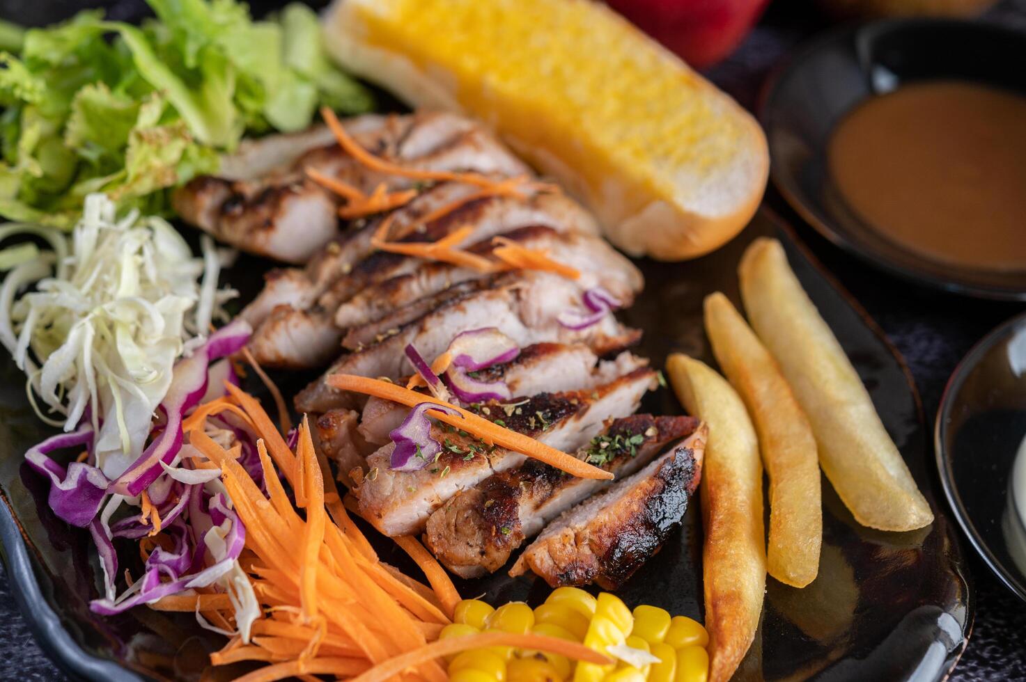 Pork steak with bread, carrots, cauliflower, lettuce and corn on a black plate. photo