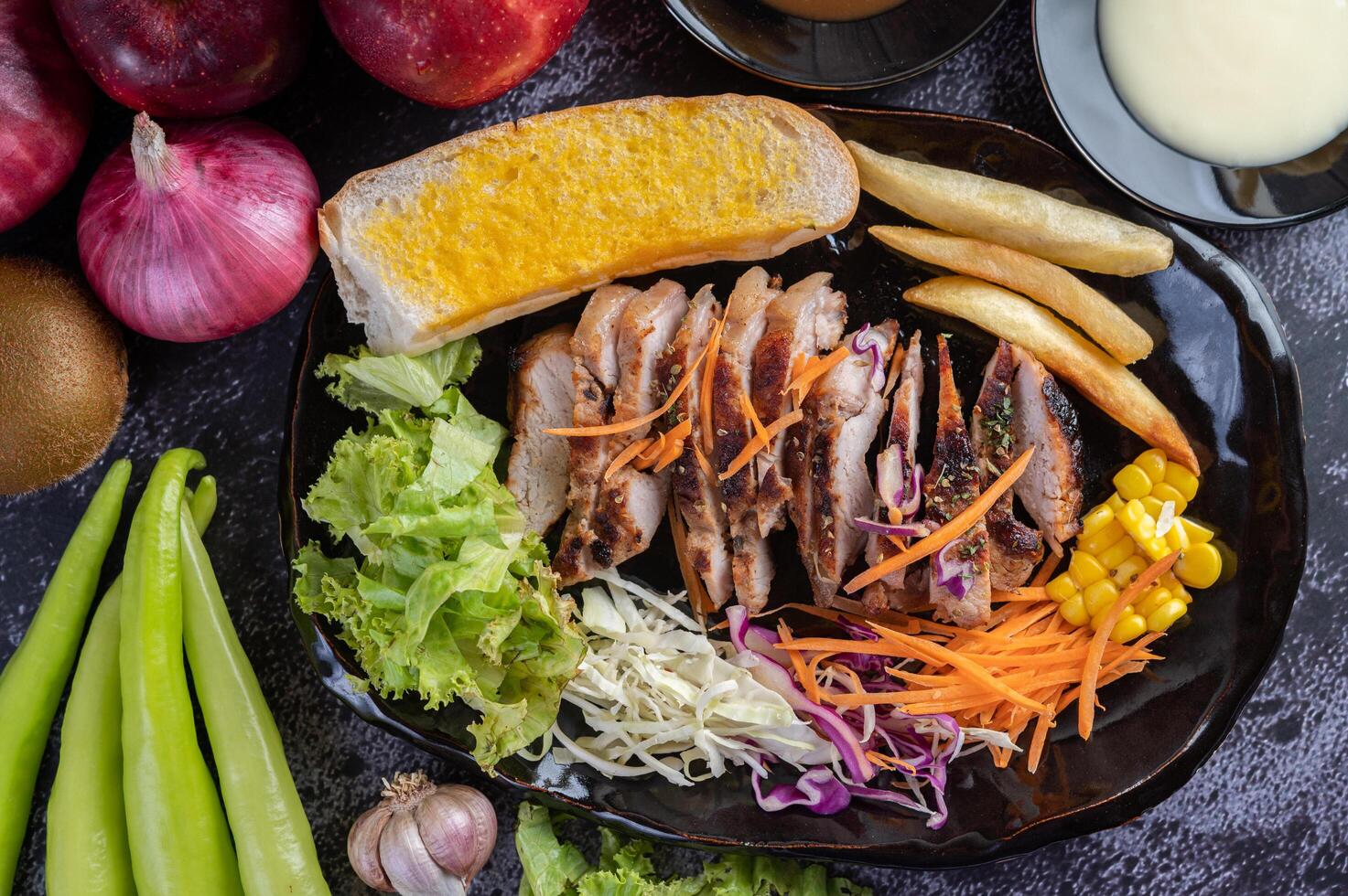 bistec de cerdo con pan, zanahorias, coliflor, lechuga y maíz en un plato negro. foto