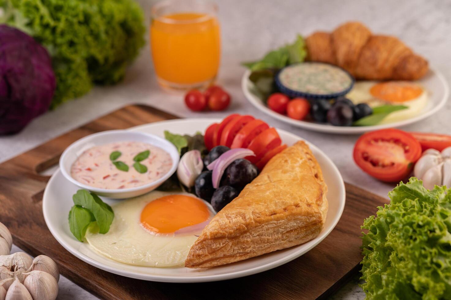 Breakfast consists of bread, fried egg, salad dressing, black grapes, tomatoes. photo