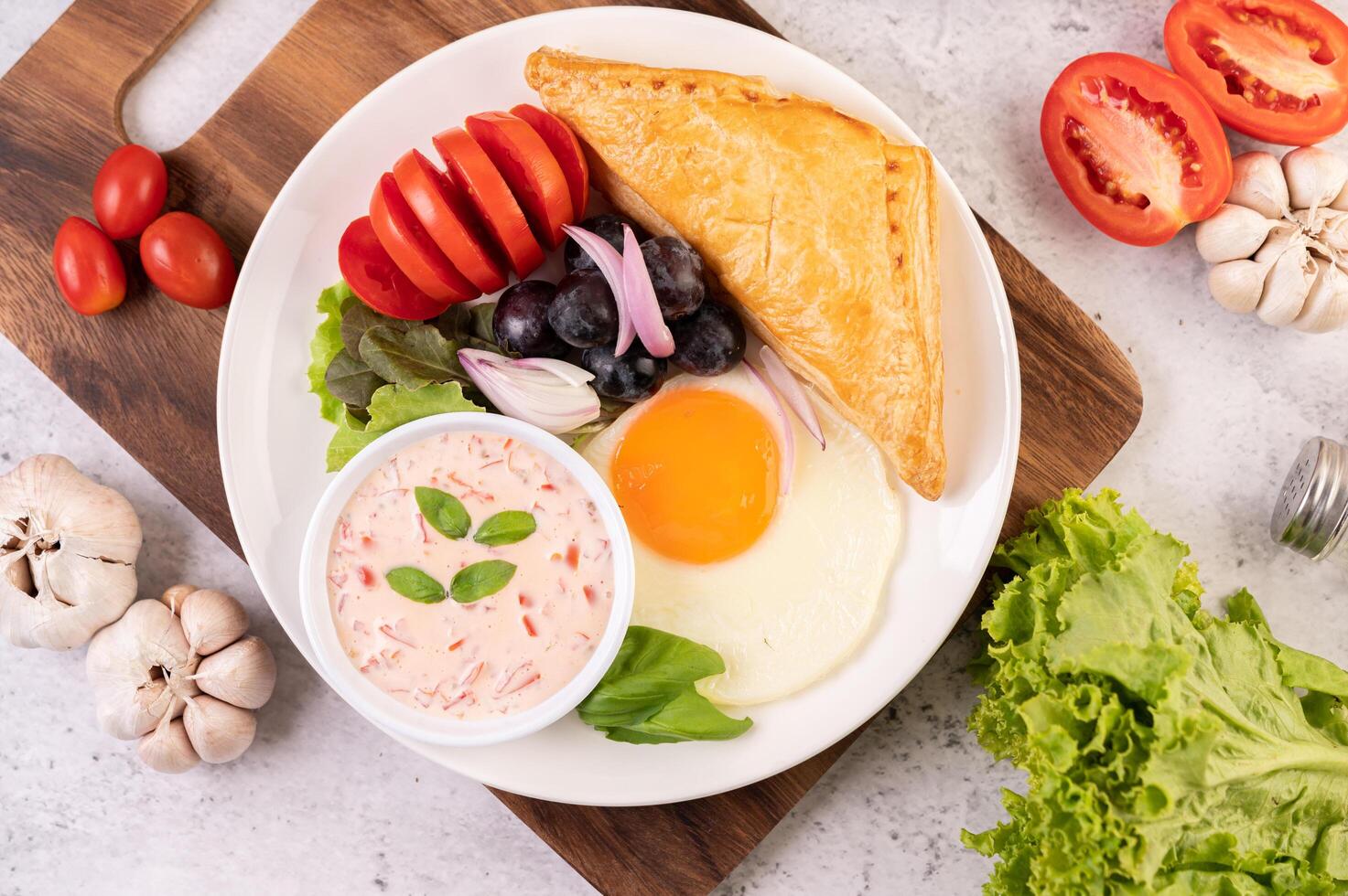 el desayuno consta de pan, huevo frito, aderezo para ensaladas, uvas negras, tomates. foto