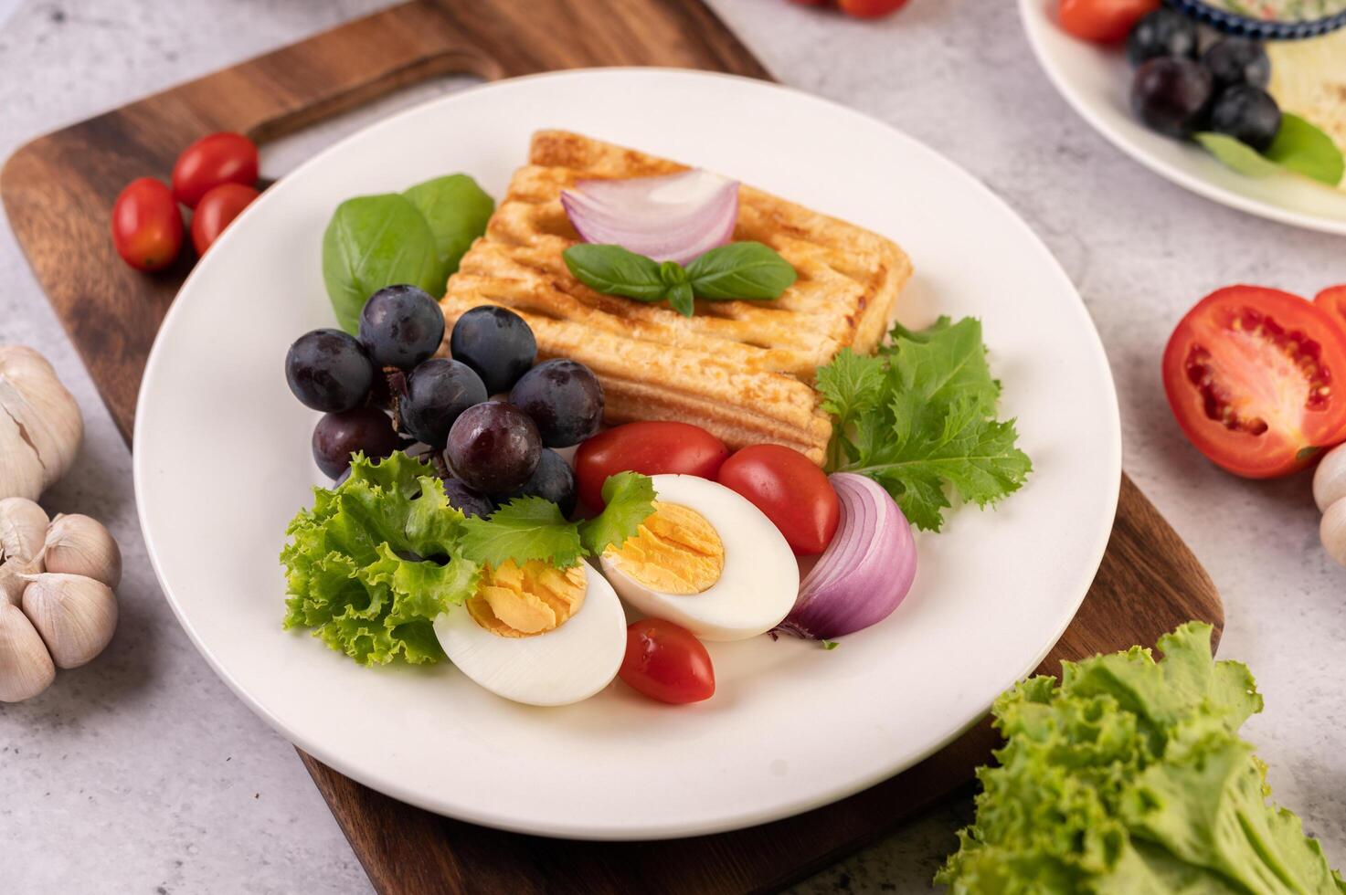 Breakfast consists of bread, boiled eggs, black grape salad dressing, tomatoes. photo