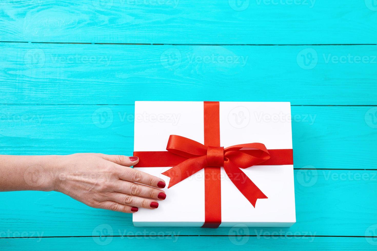 mano femenina con uñas rojas en caja de regalo sobre fondo de madera azul. vista superior y espacio de copia foto