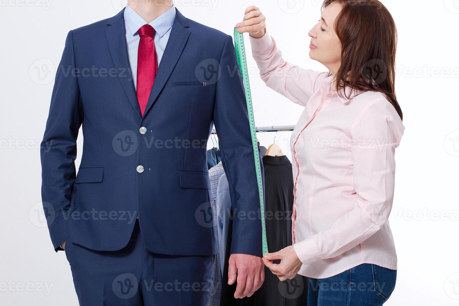 Closeup image of tailor taking measurements for business jacket suit. Businessman in red tie and blue suit at studio isolated on white background. photo