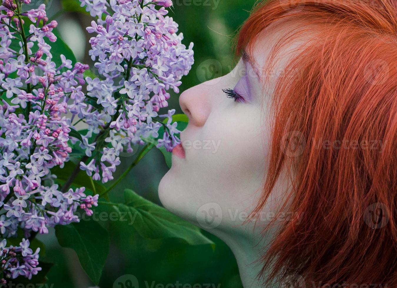 mujer joven con ramo de lilas en primavera. dama pelirroja huele flores de color púrpura. retrato de mujer atractiva en el jardín de flores. foto