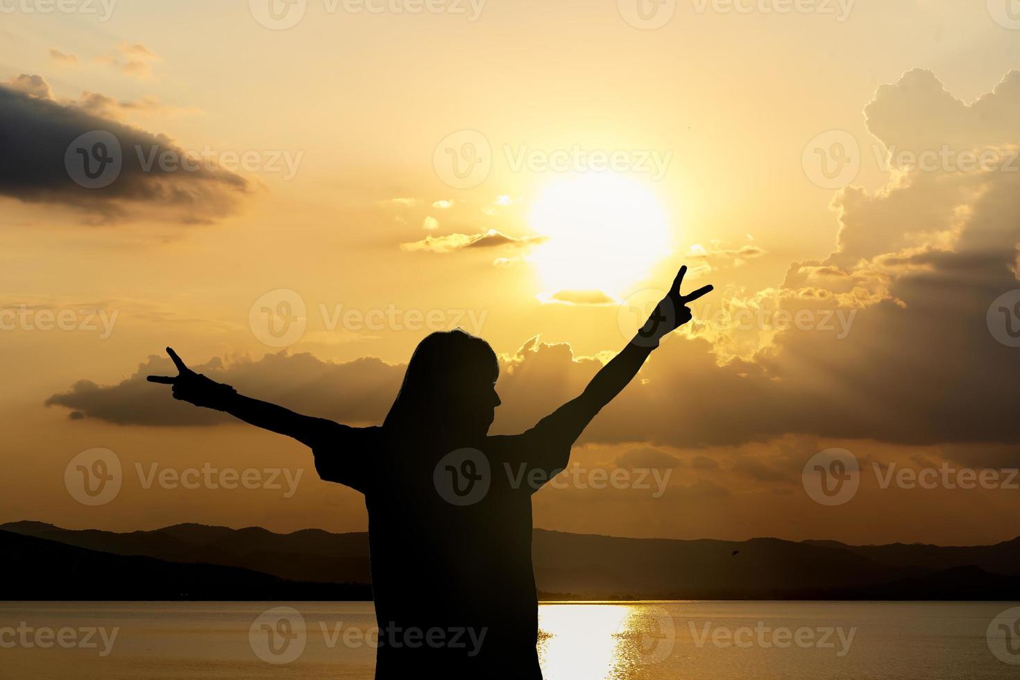 Silhouette of woman standing arms raised in the sunset. Strong female with open arms silhouette in sunrise against sun flare. Carefree person living a free life. Success freedom happy life concept. photo