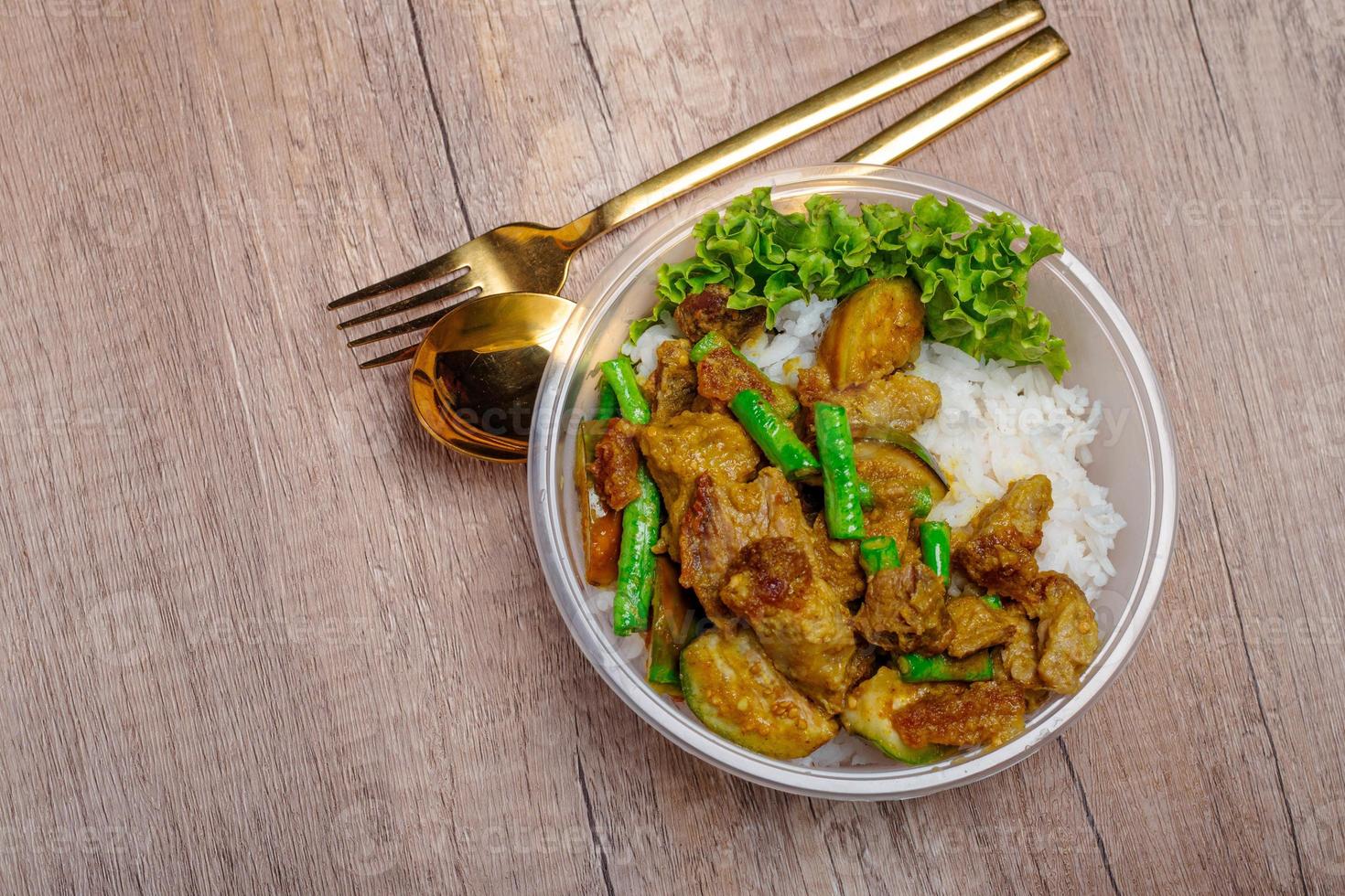 Fried crispy pork with green curry paste and vegetables in plastic cups on wooden floor photo