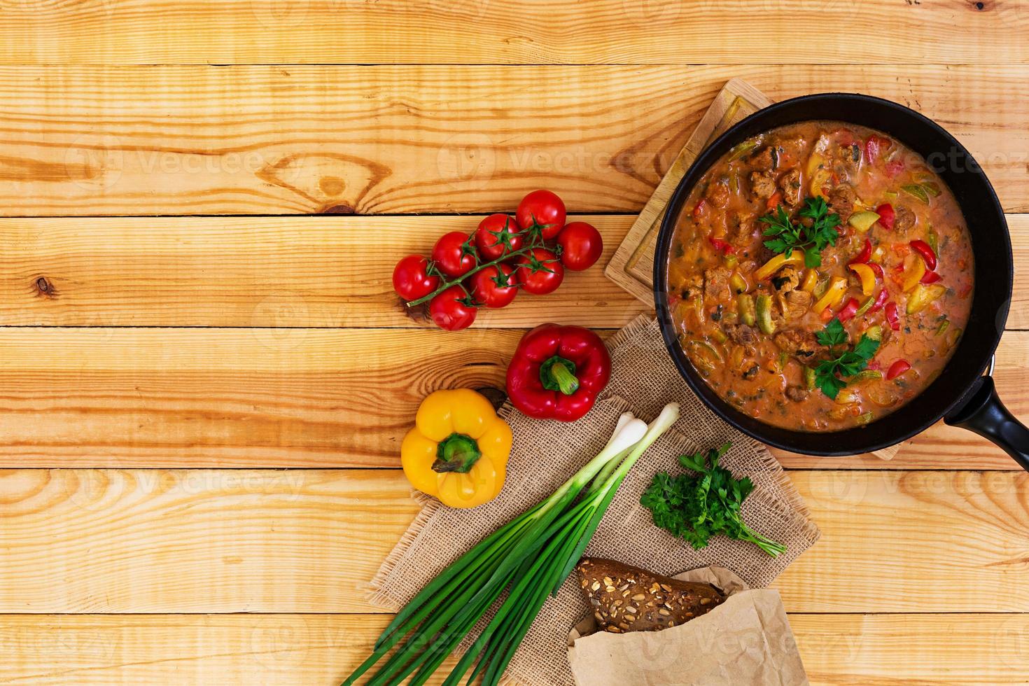 Stew with meat and vegetables in tomato sauce on wooden background. Top view photo