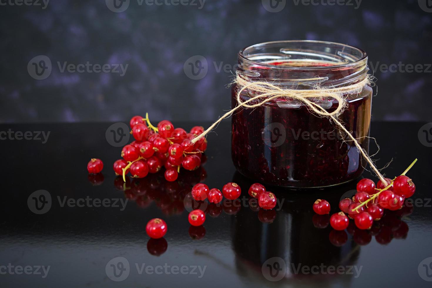Jar with jam of red currant on dark background photo