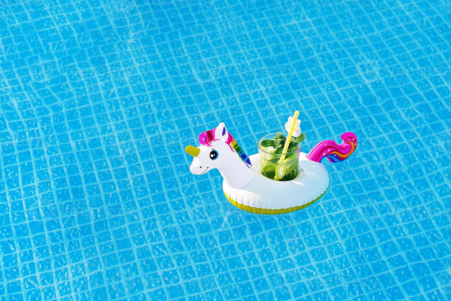 Fresh coctail mojito on inflatable white unicorn toy at swimming pool. Vacation concept. photo