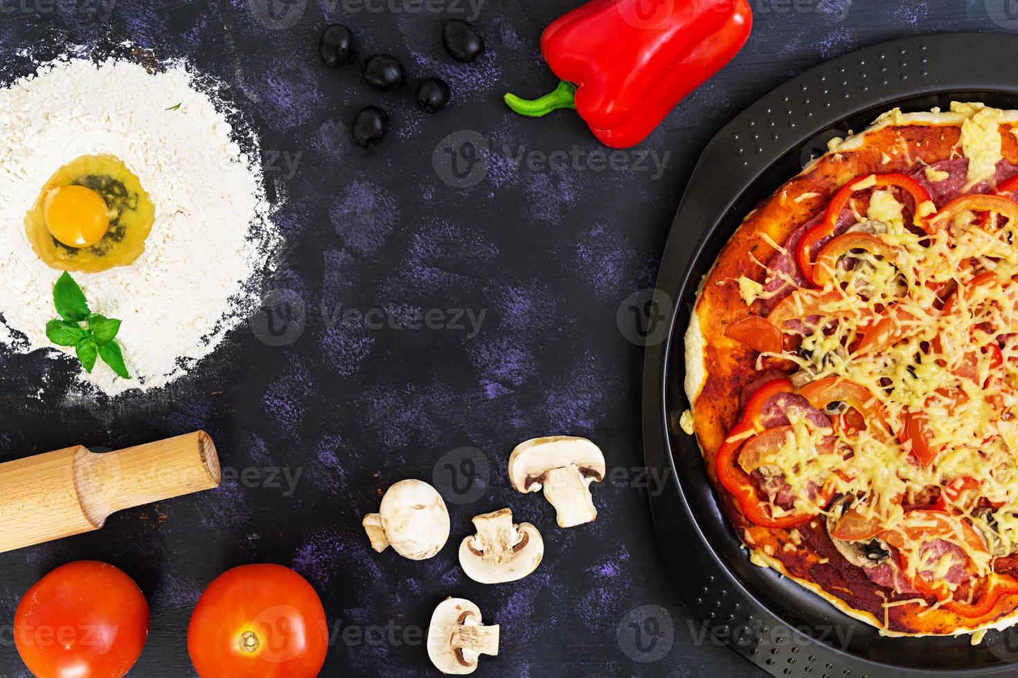 Raw pizza dough with ingredients and spices on dark background. Top view photo