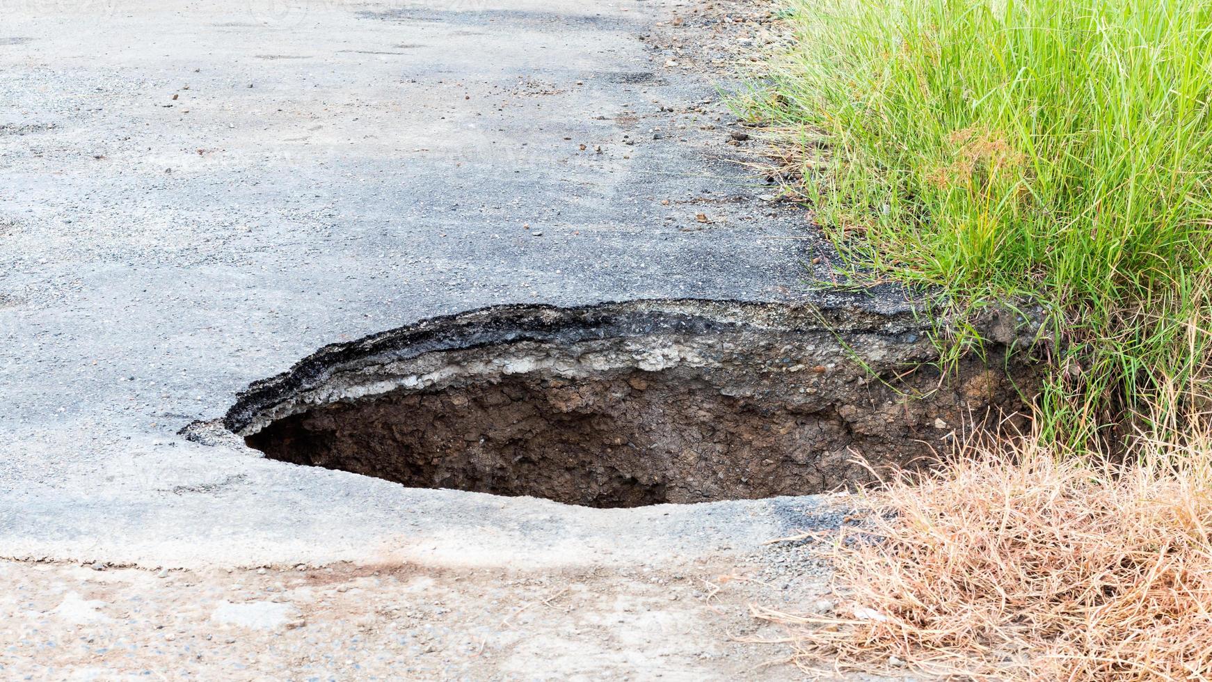 Deep hole, paved road with grass. photo